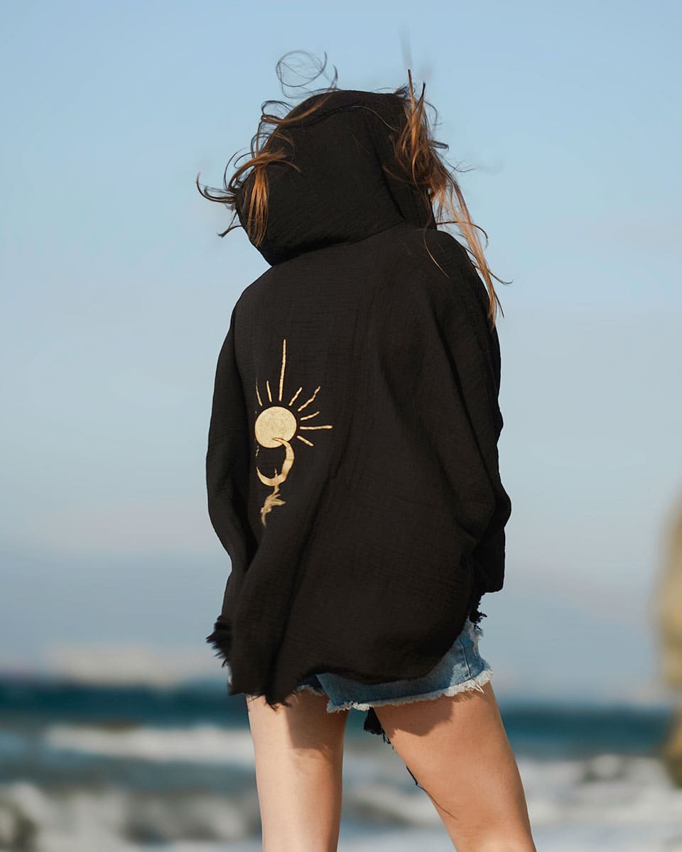 Person wearing a black hoodie with a sun design on the beach