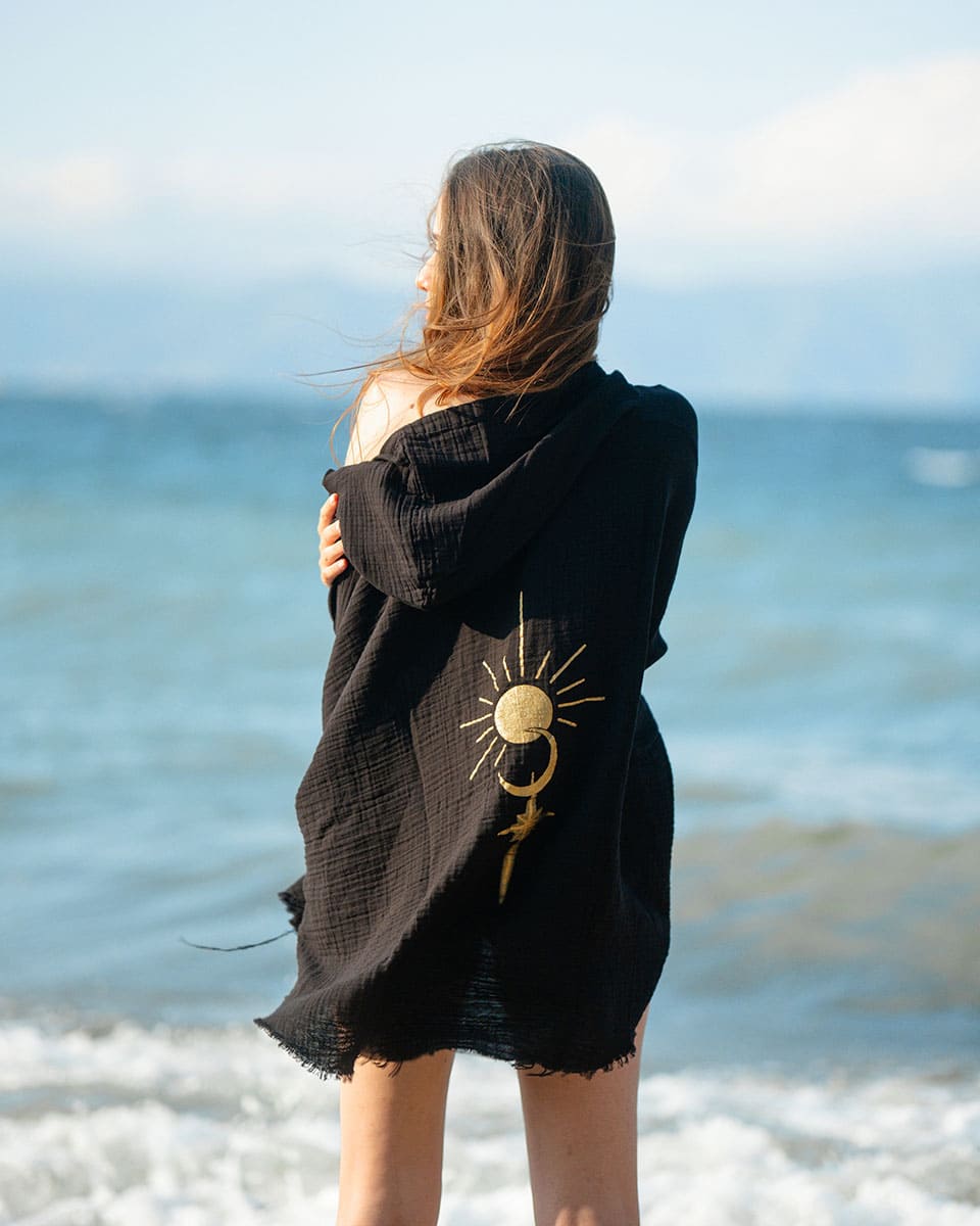 Person wearing a black robe with a sun and moon design on a beach