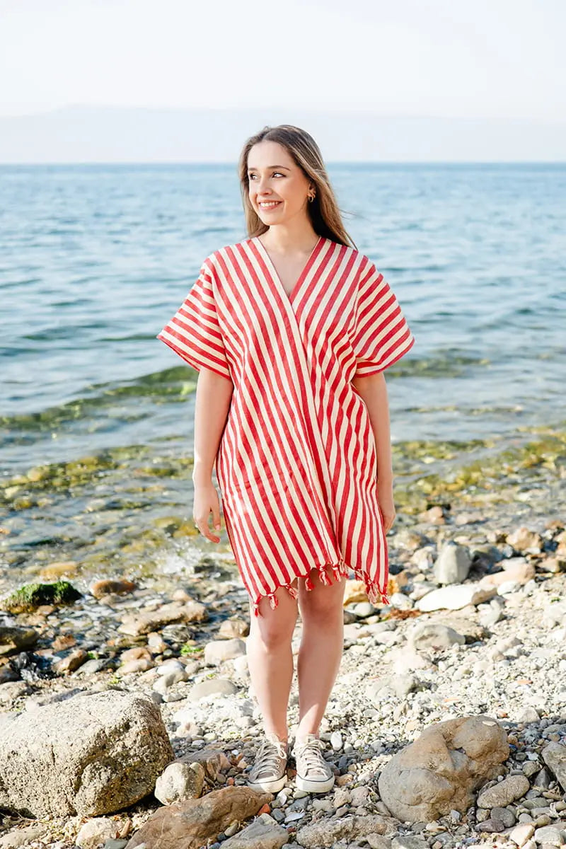 Woman wearing a red and white striped swimsuit cover up standing on a rocky beach.