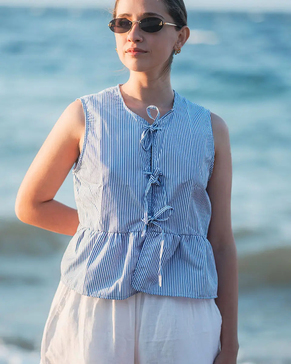 Woman wearing a blue striped sleeveless top and sunglasses with a blurred ocean background