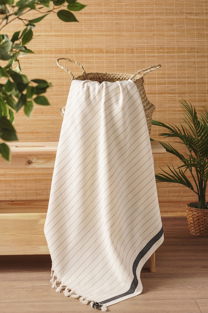 white towel with black trim draped over a woven basket against a wooden wall.