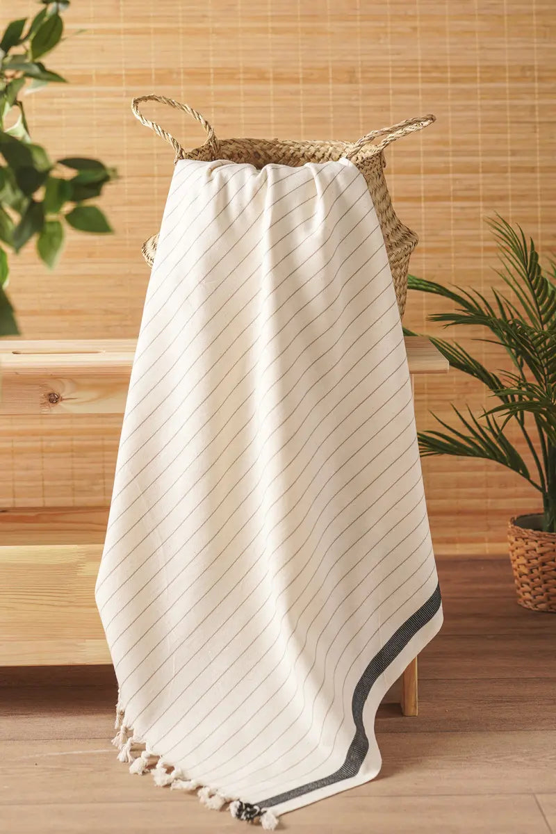 white towel with black trim draped over a woven basket against a wooden wall.