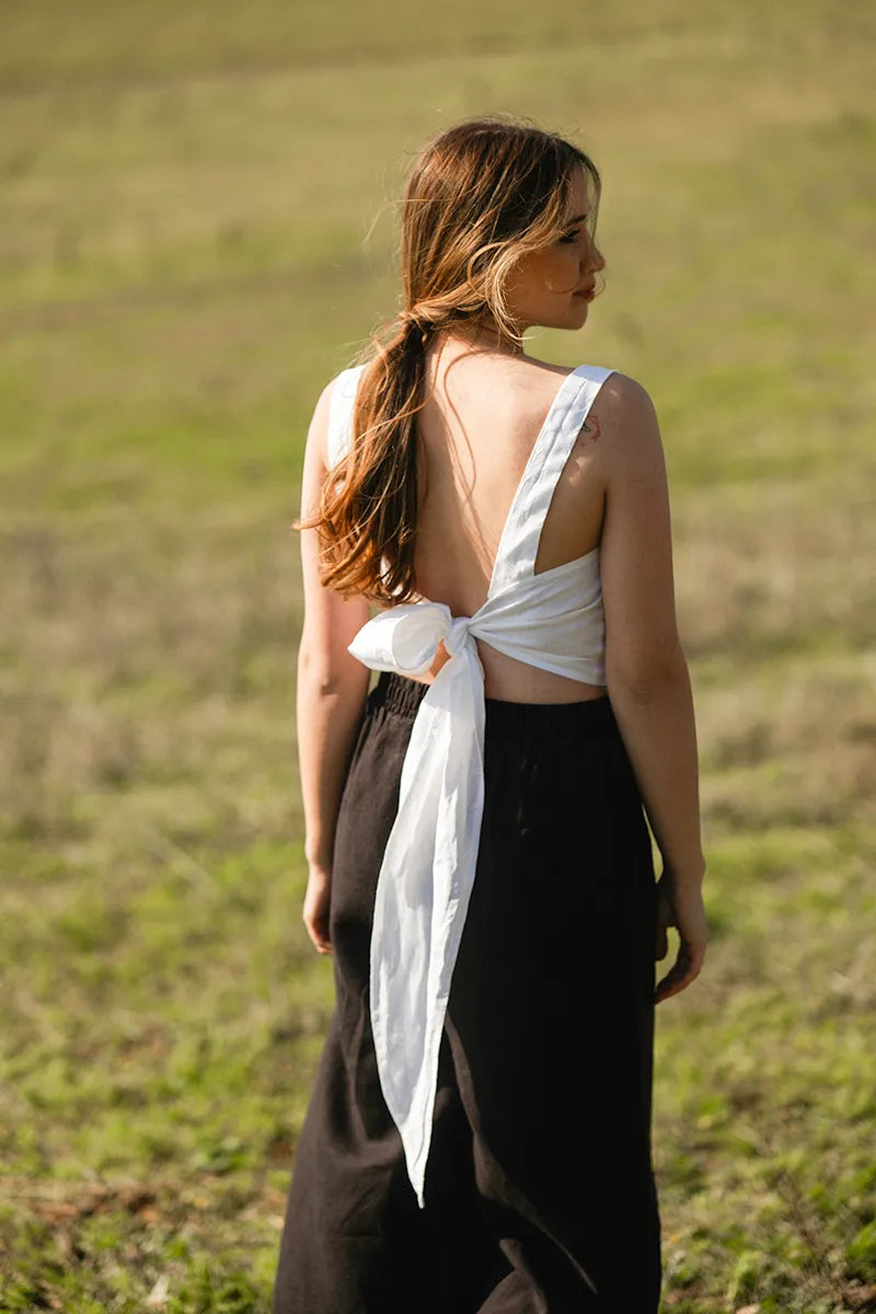 Woman in a white linen tie back top and black pants standing in a grassy field