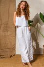 Woman in a white tank and white linen wide leg pants by a beige wall — European Flax linen with an airy drape