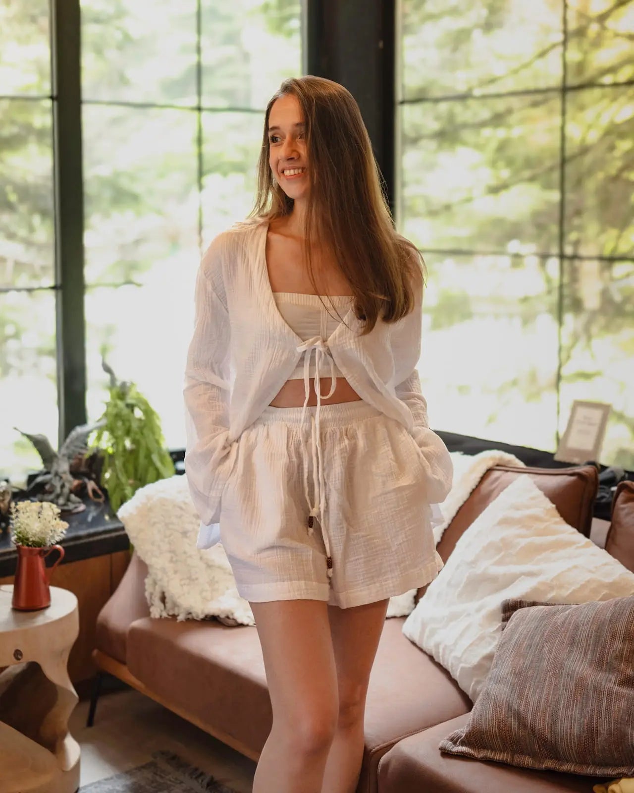 Woman in a White Loungewear Set standing in a sunlit room with large windows.