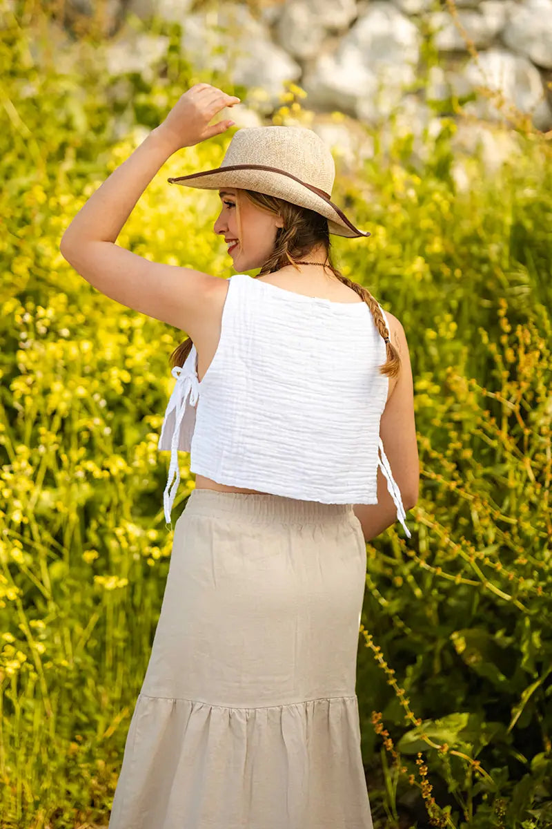 Woman in a white top and beige skirt standing in a field of yellow flowers.