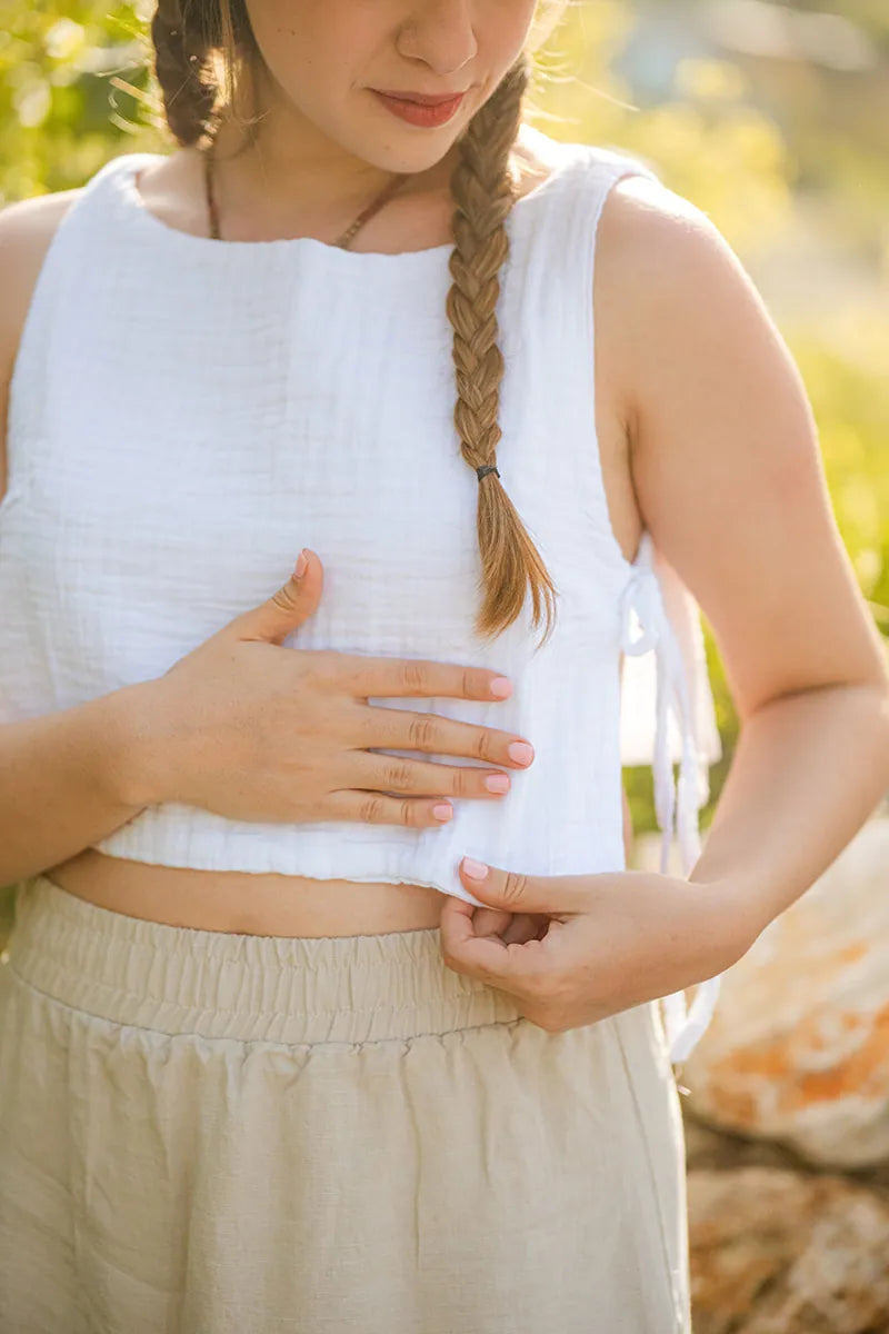 Woman wearing a white sleeveless top and beige pants with braided hair, standing outdoors.