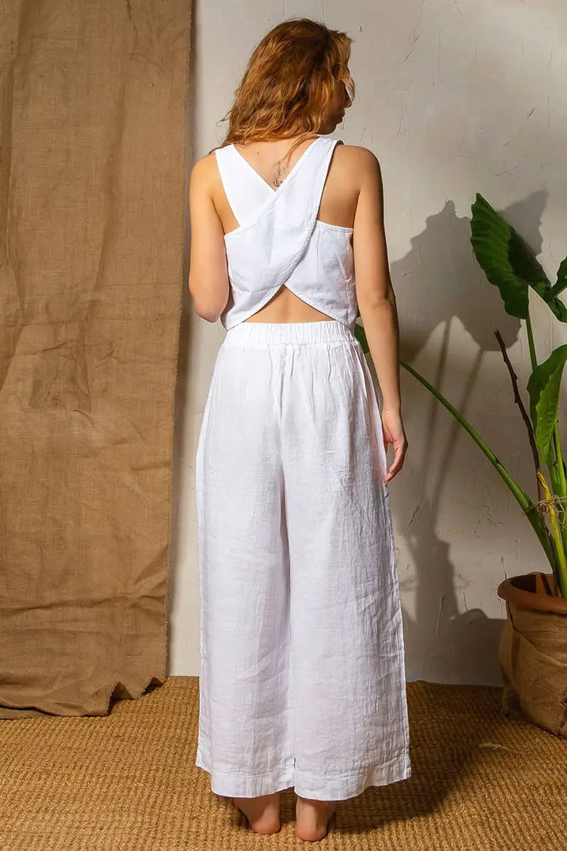 Woman wearing a White Wide Leg Pants with a backless design, standing against a neutral wall with a plant to the side.