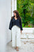 Full body view of black asymmetric linen top styled with light trousers.