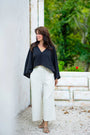 Full body view of black asymmetric linen top styled with light trousers.
