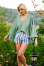 Full body view of green asymmetric linen top styled with shorts in nature setting.