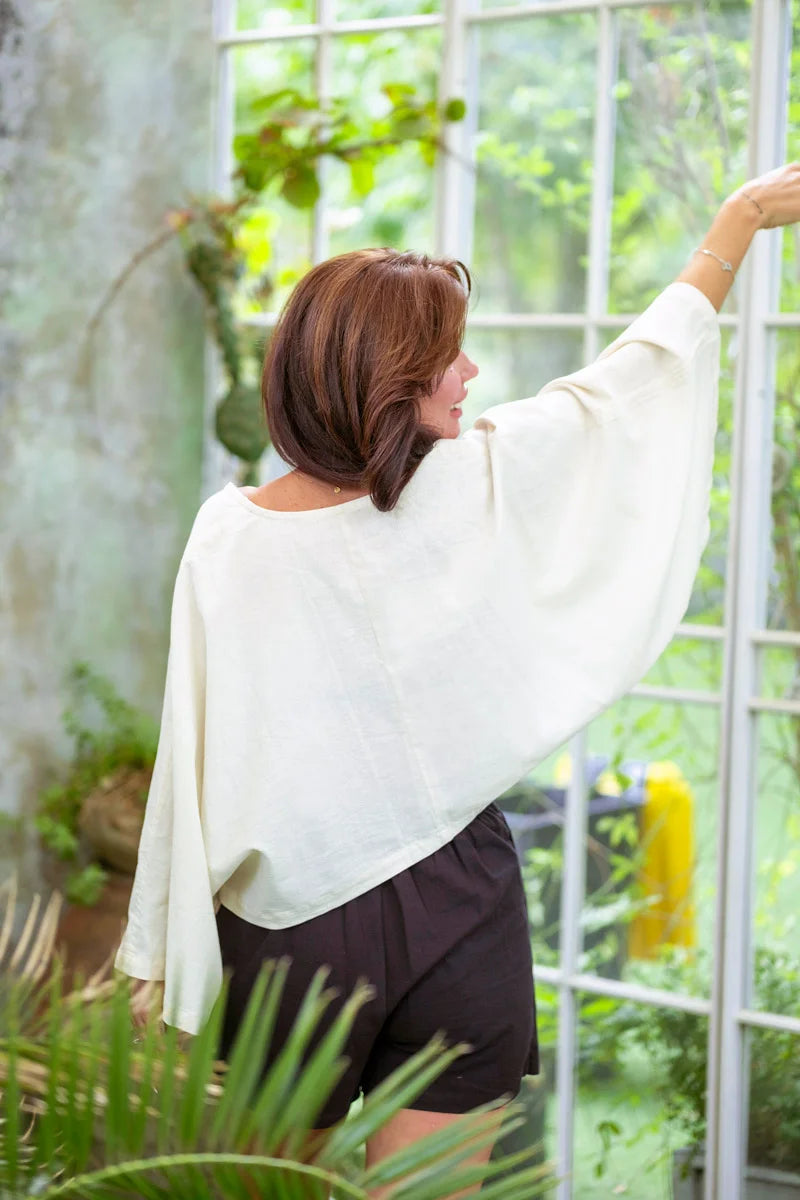 Back view of white asymmetric long sleeve linen top with poncho silhouette.