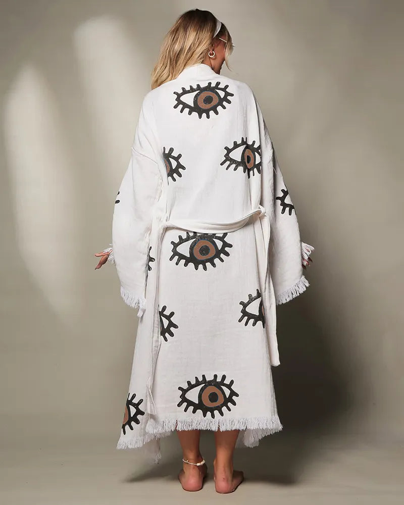 Woman wearing a white robe with brown eye patterns on a neutral background