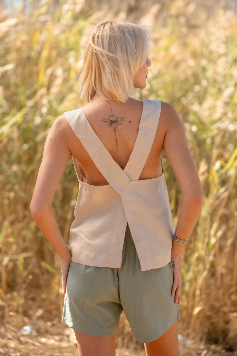 Woman wearing a beige linen sleeveless  cross back top, standing in a field of tall grass.