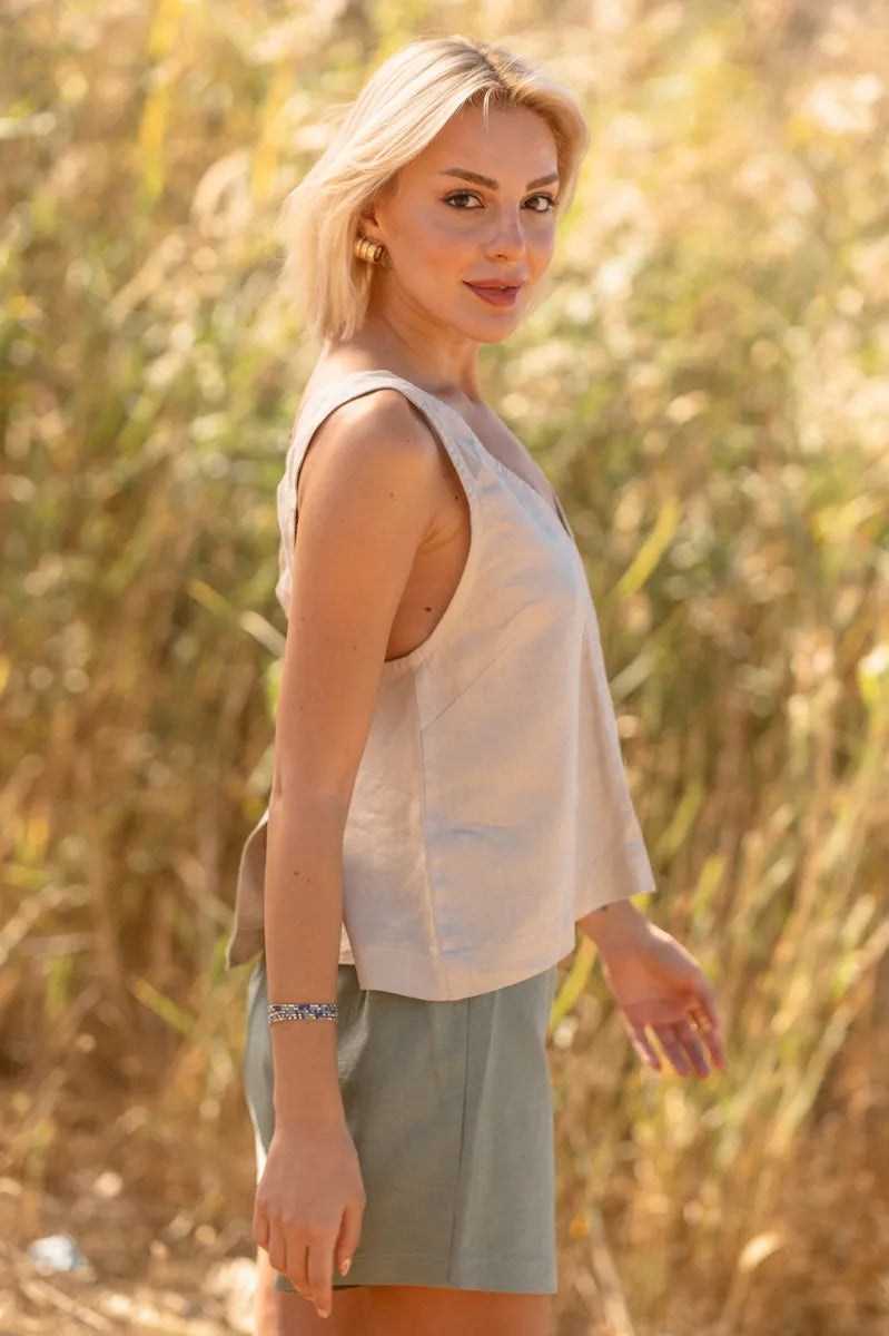 Woman standing in a field wearing a beige linen sleeveless tank top and green shorts.