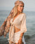 Woman on a beach wearing a beige top and white shorts with a patterned headscarf.