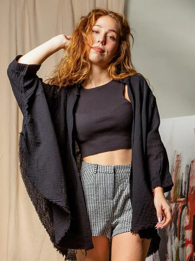 Woman wearing a black muslin robe and checkered shorts with a dark jacket in a casual setting.