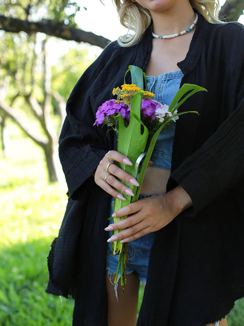 Person wearing open front black cardigan and holding a bouquet of flowers outdoors