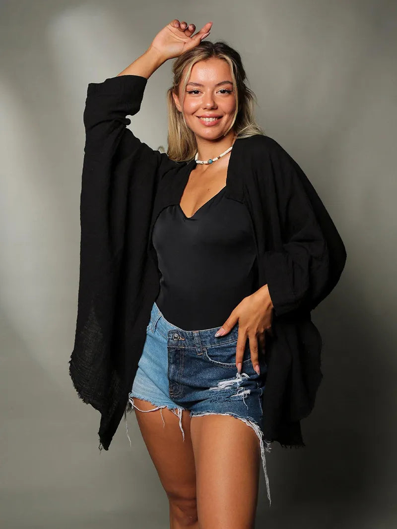 Woman wearing a black cardigan, black top, and denim shorts against a neutral background