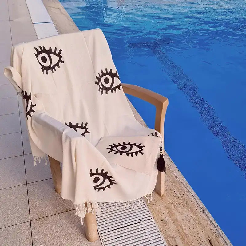 white turkish cotton towel with evil eye designs draped over a chair by a pool