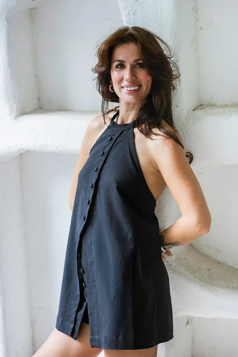 Woman wearing a black sleeveless dress against a white stone wall.