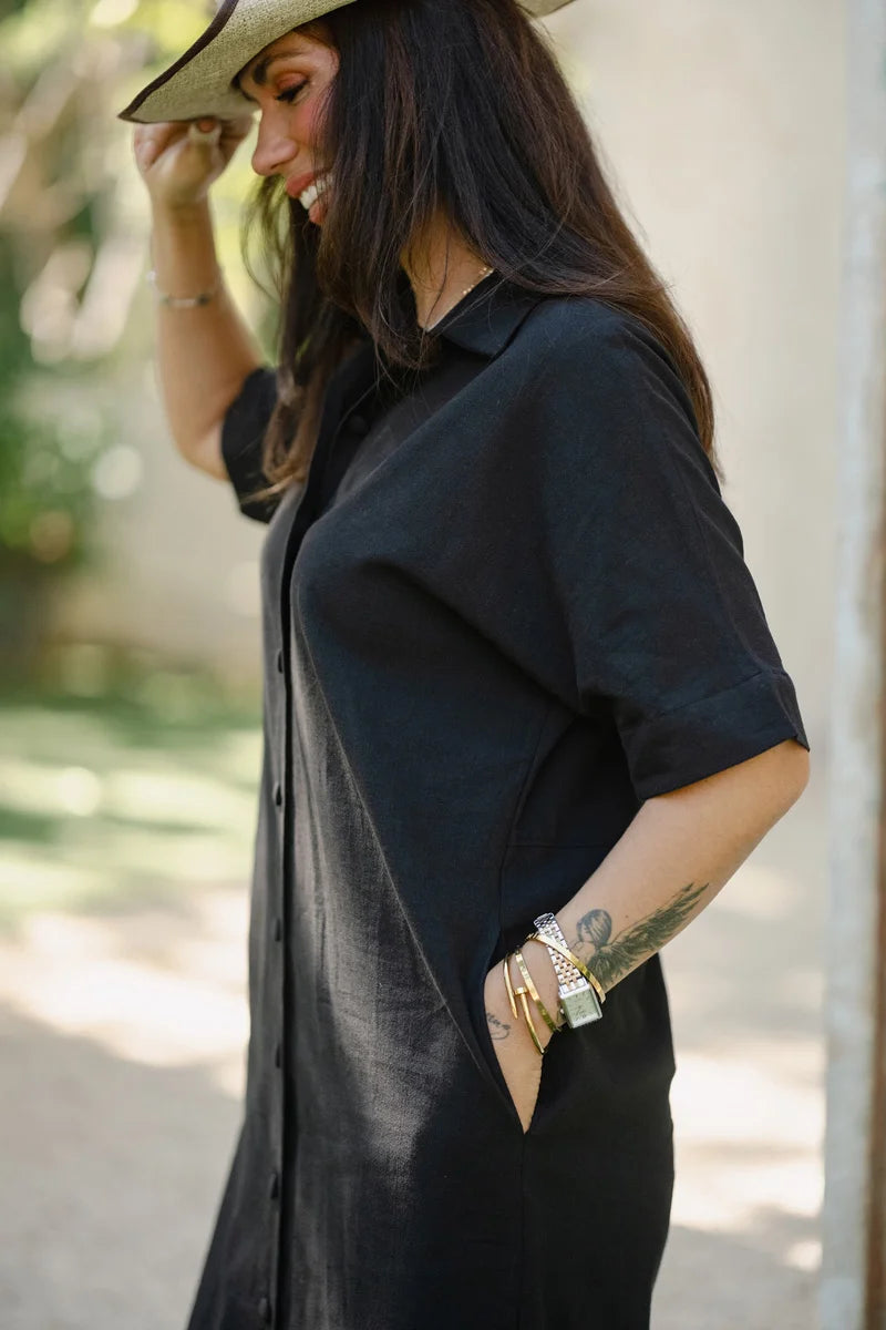 Woman wearing a black shirt dress outfit with a hat, standing outdoors.
