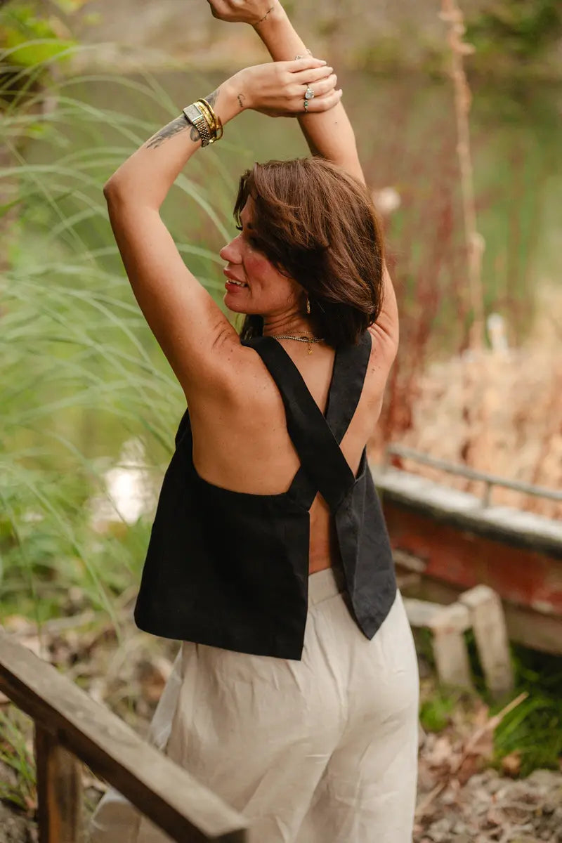 Woman in a black Linen Wide Strap Tank Top and white pants standing outdoors with greenery in the background