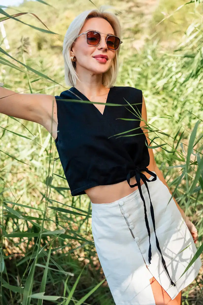 Woman wearing a black sleeveless linen vest top and light-colored pants standing in a grassy area.