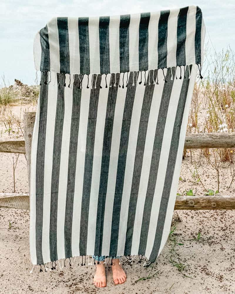 A woman grasping a beach towel with black and white stripes