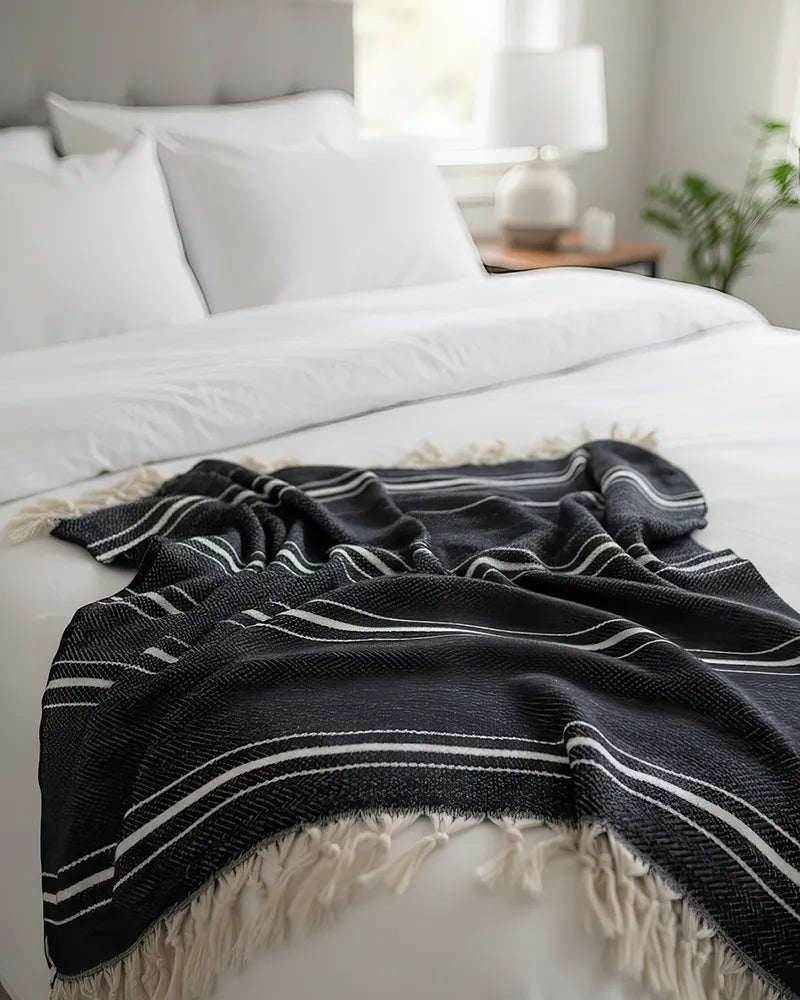 Black striped blanket on a white bed in a bedroom setting