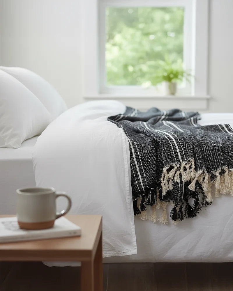 Bed with a black and white striped blanket, white pillows, and a wooden side table with a mug and book.