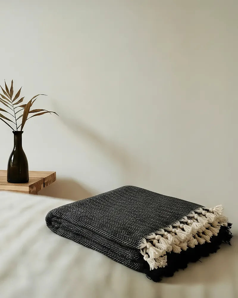 Black textured throw blanket on a bed with a minimal background