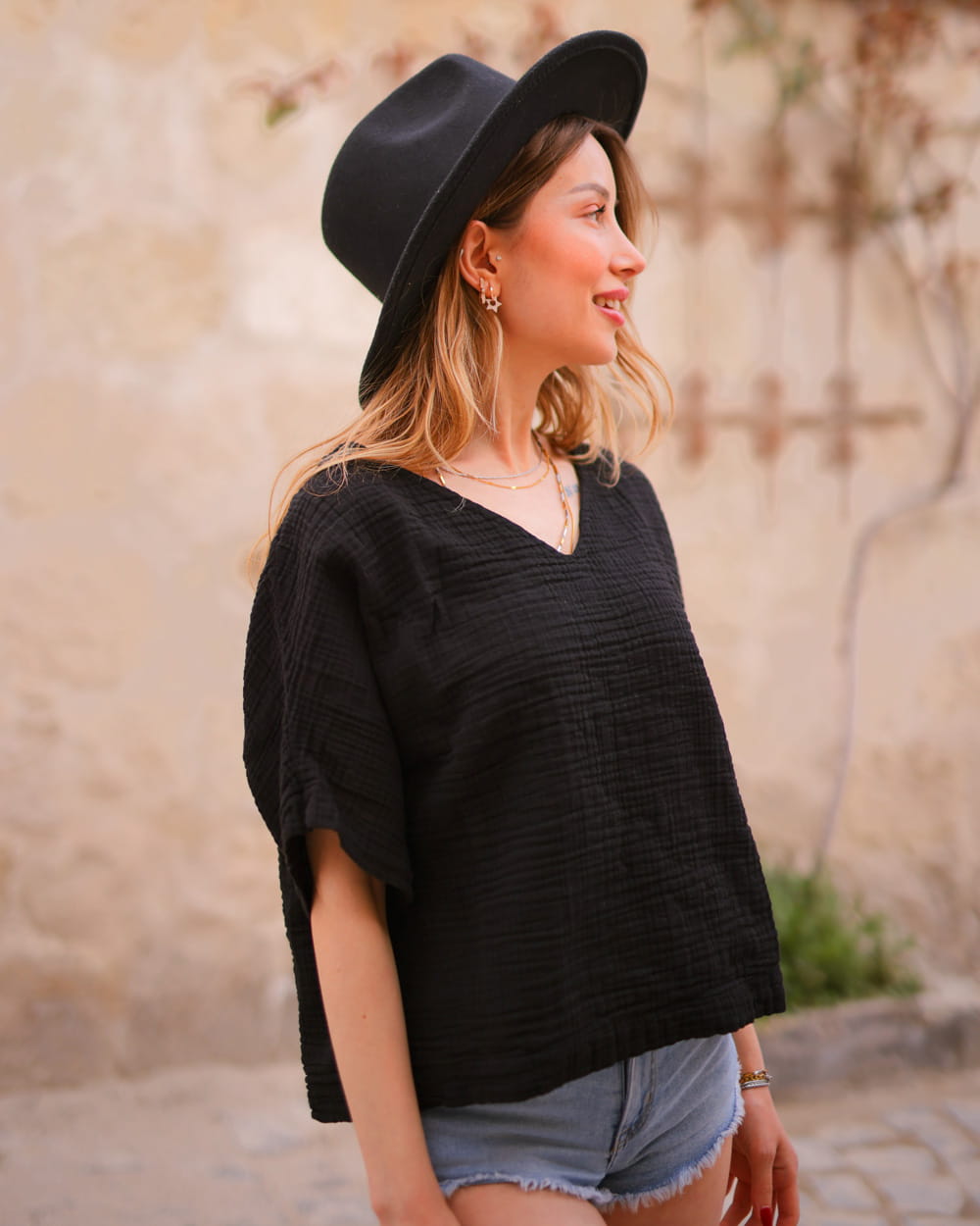 Woman wearing a black hat and black muslin cotton tshirt with denim shorts outdoors.