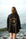 Person wearing a black cardigan with a gold eye design by the water