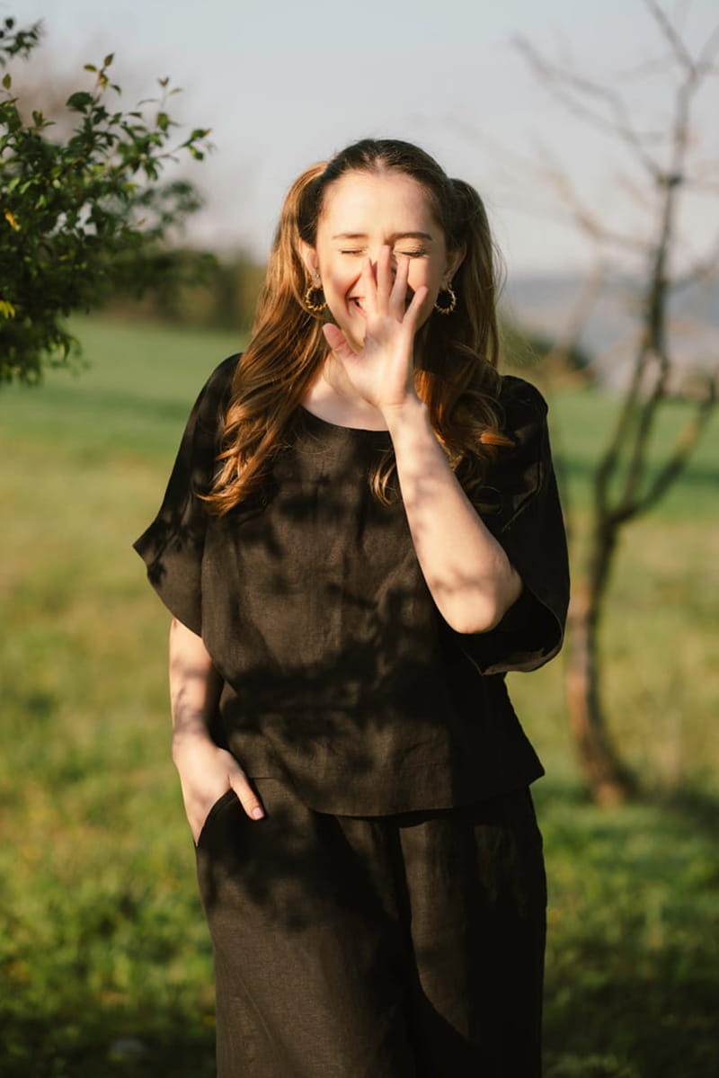 Woman in a black linen blouse standing outdoors with trees and grass in the background