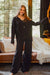 Woman in a black muslin loungewear set standing in a room with a couch and window