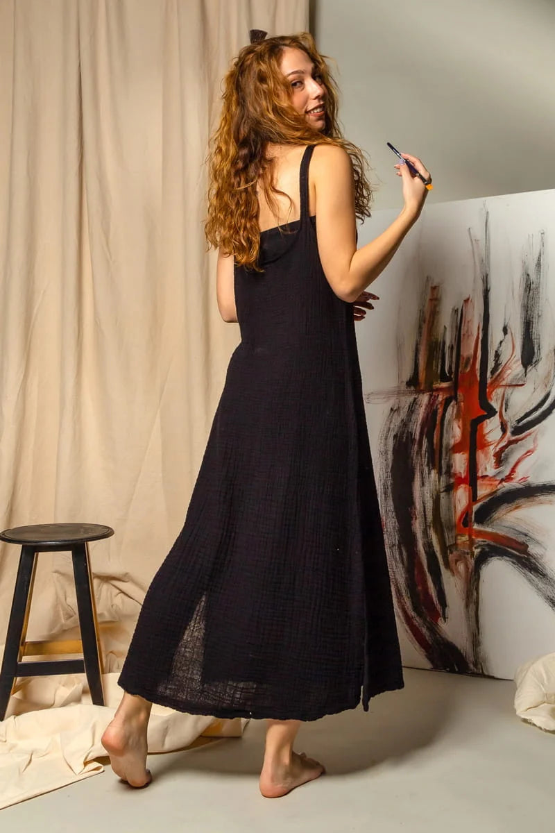 Woman in a black open back maxi  dress painting on a white canvas with abstract art in the background.
