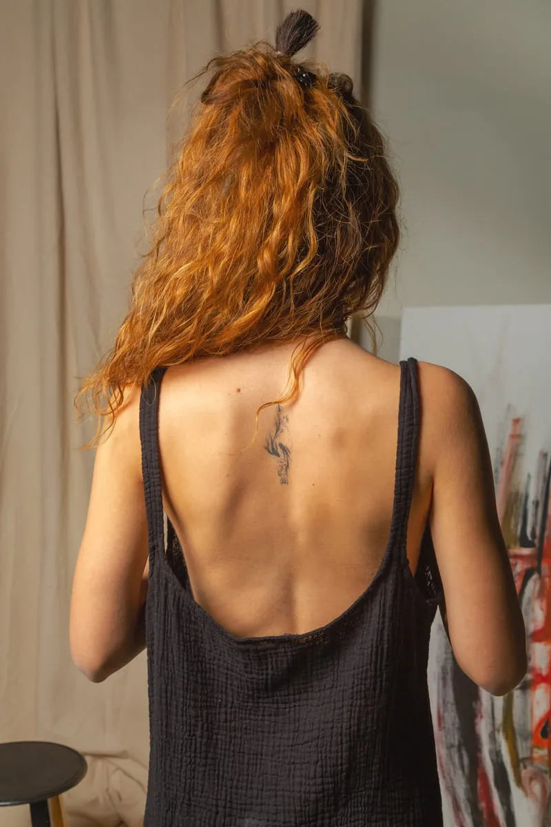Person with red hair wearing a black sleeveless dress, standing indoors.
