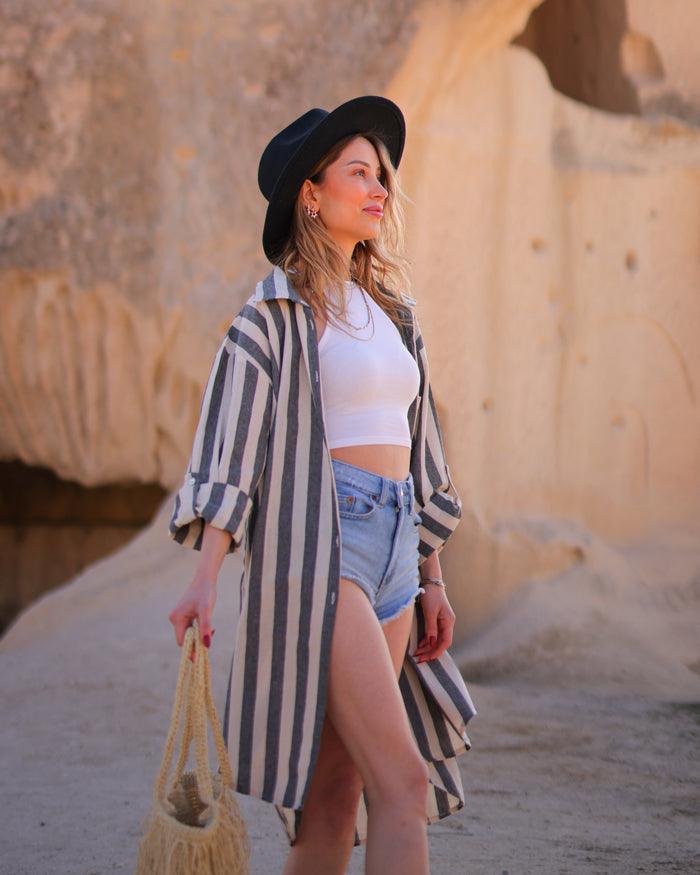 A woman wearing a black striped shirt and shorts poses in front of a striking rock formation.