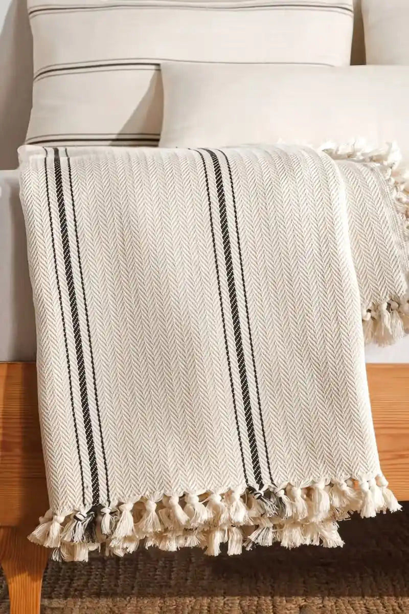 cream throw blanket with black stripes and tassels draped over a chair.
