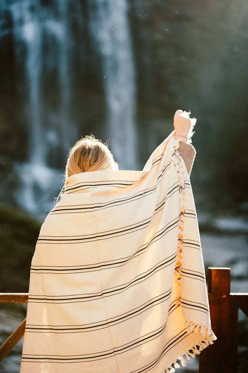 Person wrapped in a striped outdoor blanket standing in front of a waterfall