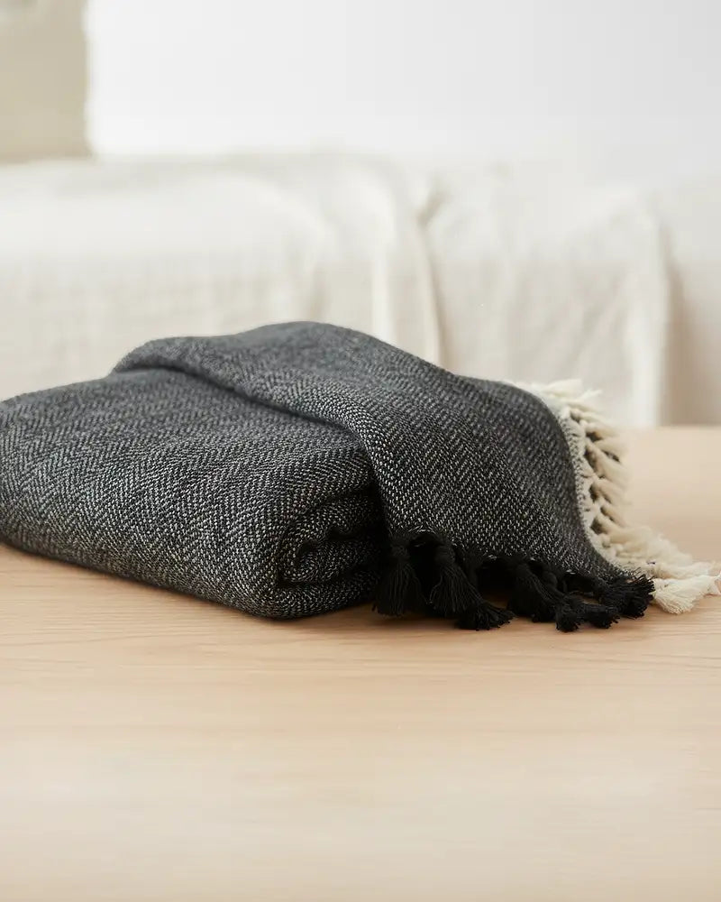 Folded black blanket with white tassels on a light-colored couch.
