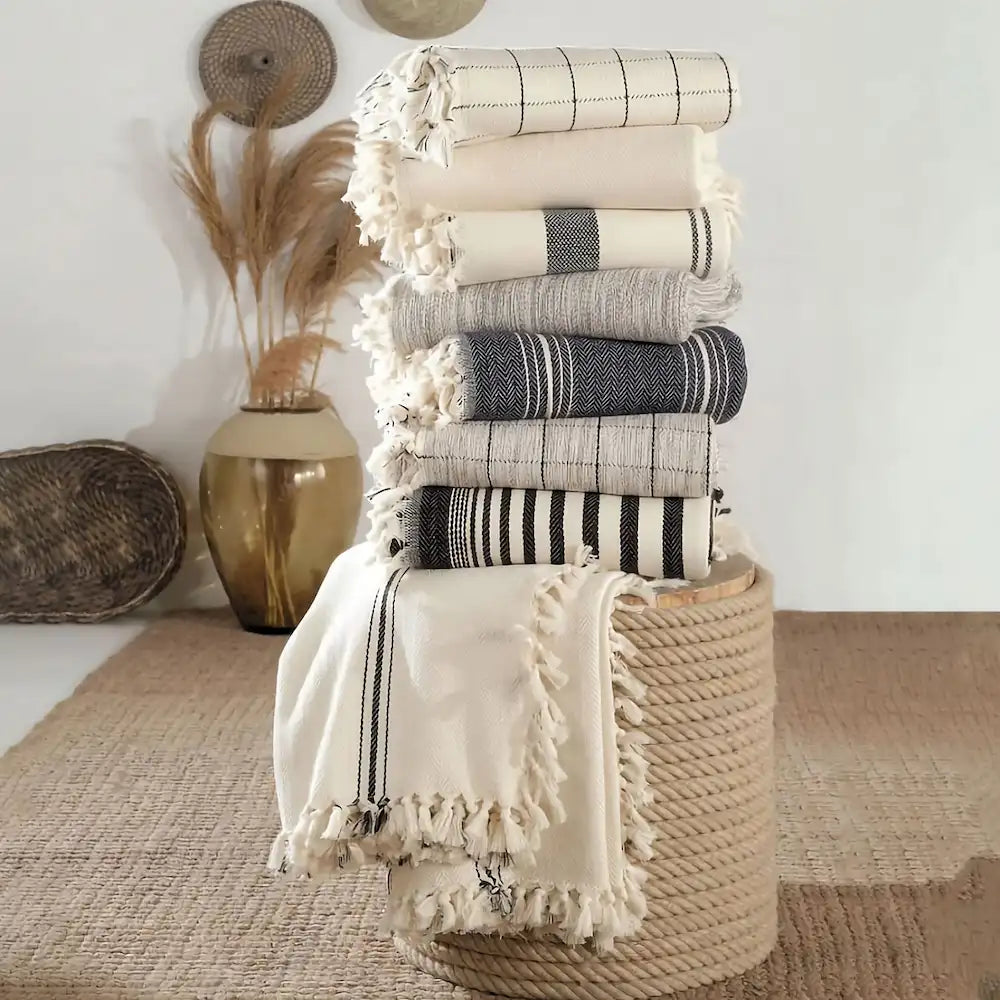 Stack of folded towels on a woven stool with decorative items in the background