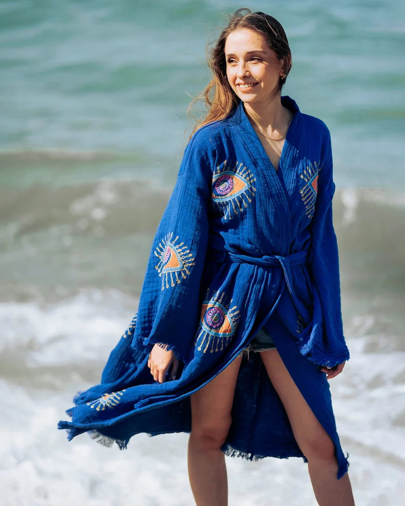 Woman wearing a blue robe with eye pattern on a beach