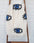 An off-white woven throw blanket with a black and blue eye pattern, draped over a wooden ladder against a white brick wall. #Color_Blue_Eye_Blanket