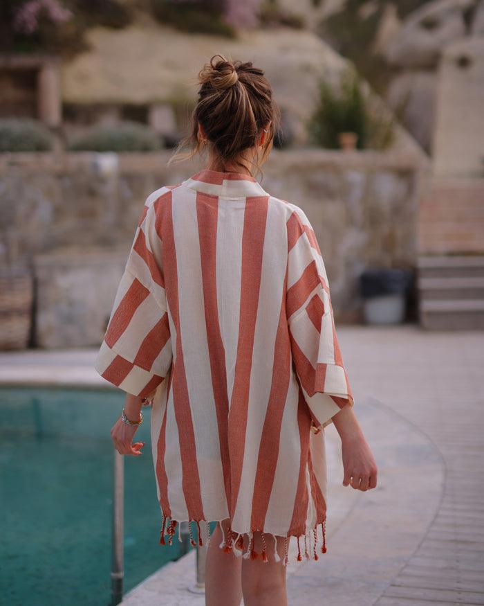 A woman in a striped robe walks by a pool, elegantly displaying her boho swimsuit cover-up.