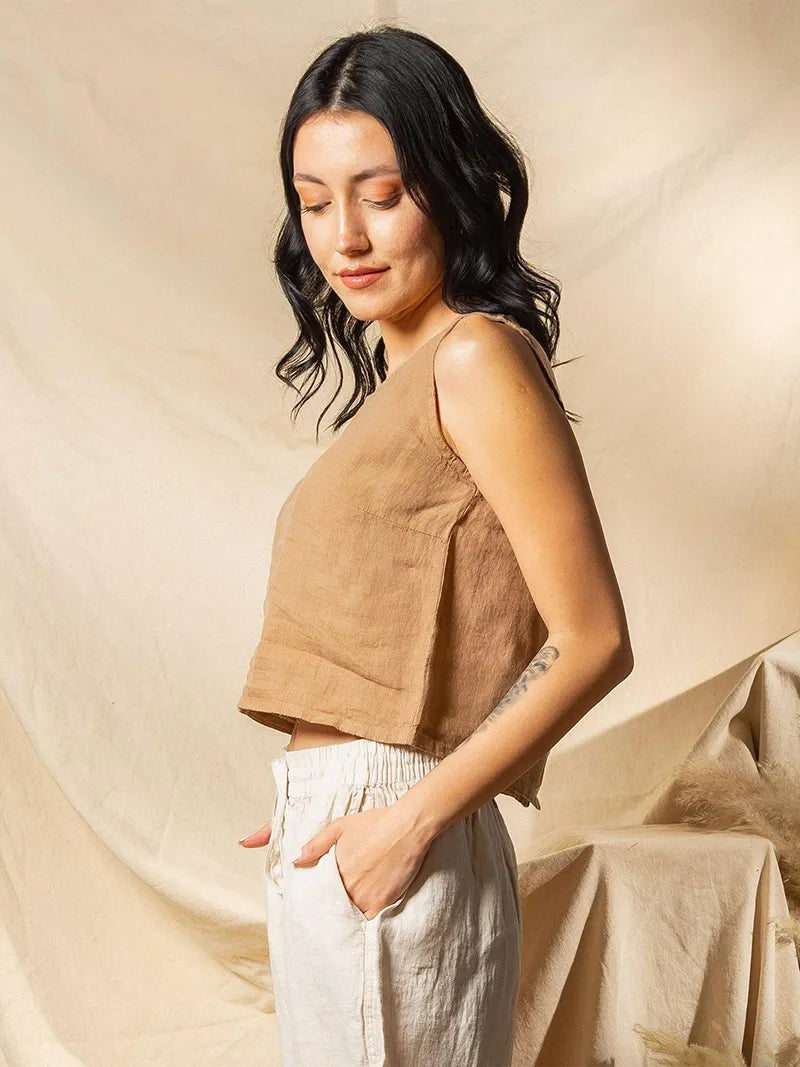 Woman wearing a brown sleeveless top and white pants against a beige background