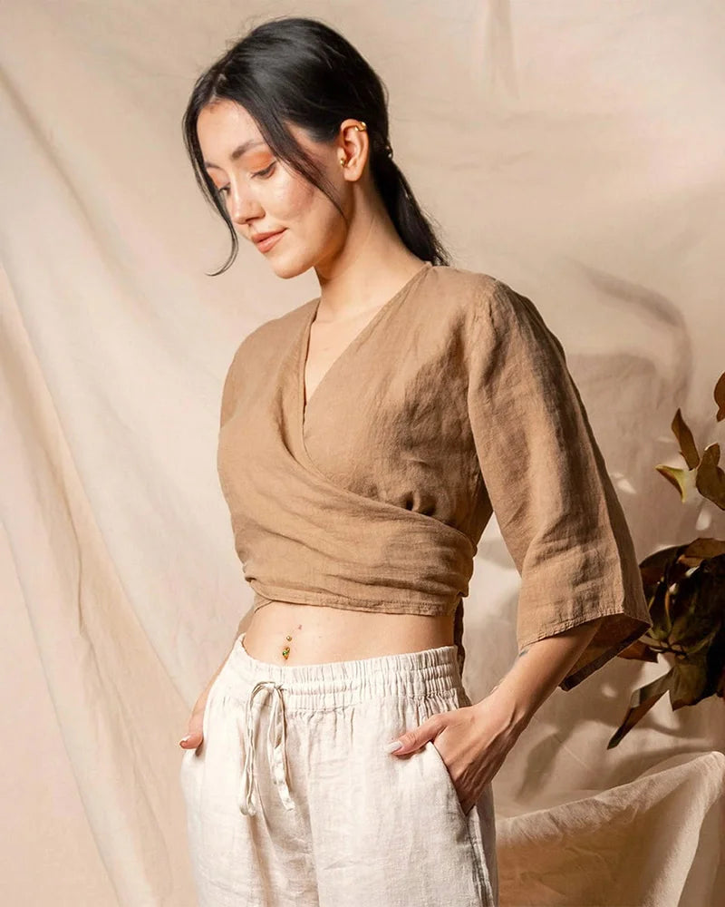 Woman wearing a browntie back linen  top and white pants against a beige background