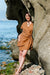 Woman in a brown wrapp dress standing among rocks by the ocean