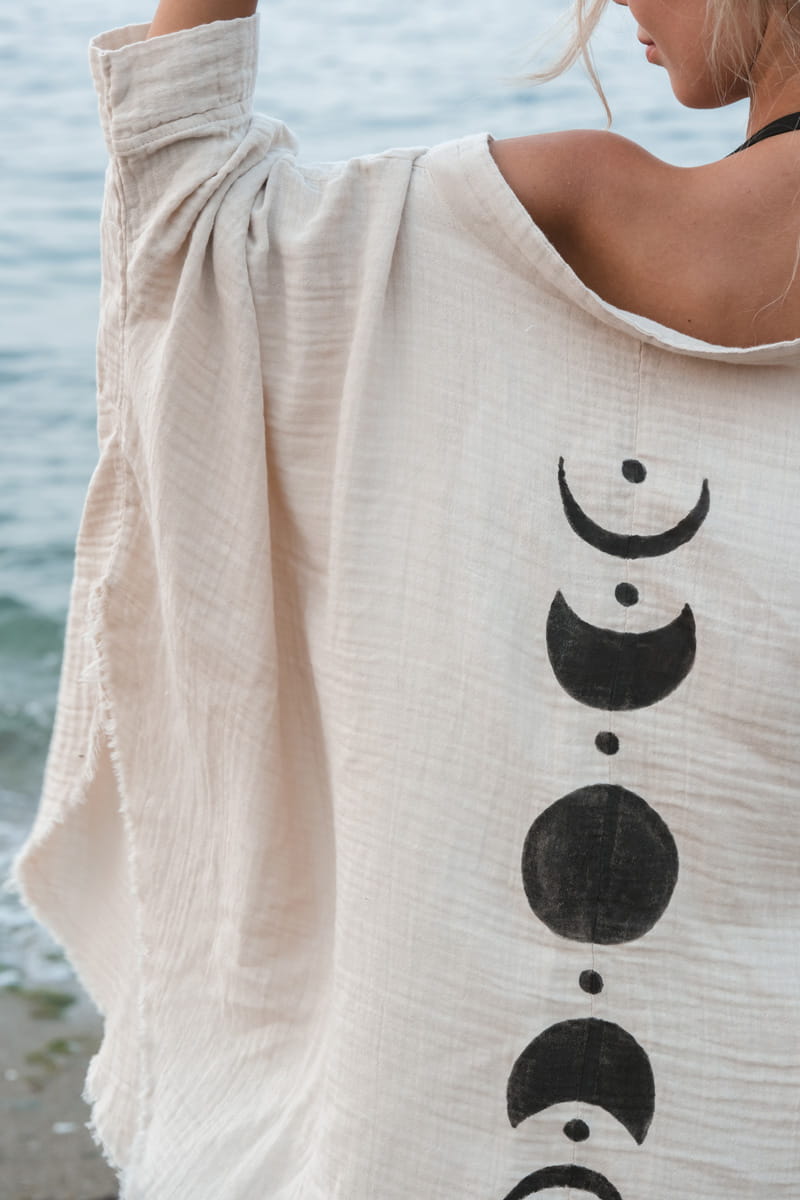 Beige cardigan with black moon phase design worn by a person by the water.